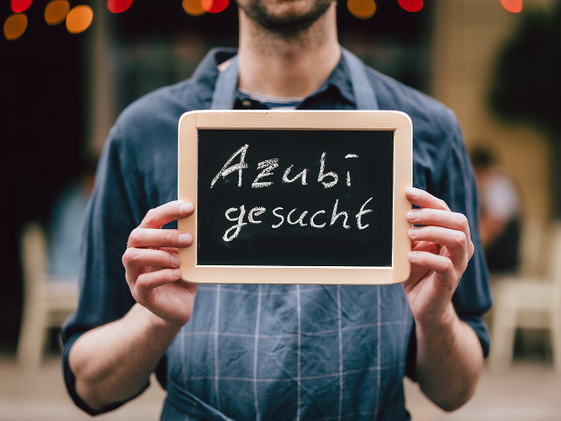 Eine Person hält eine kleine Tafel in den Händen auf der "Azubi gesucht" geschriebenn ist