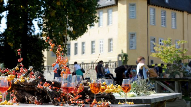 Weingläser stehen auf einem Tisch, im Hintergrund ist das Schloss Dyck zu sehen