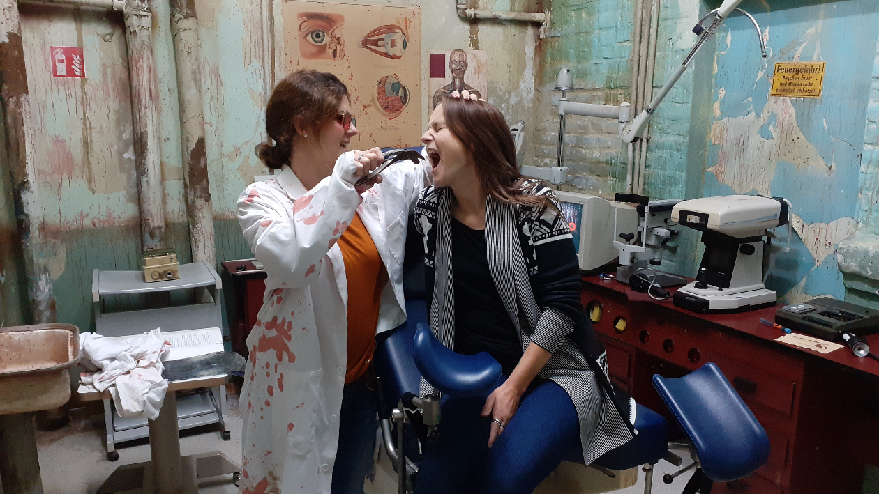 Anke und Sandra sitzen auf einem Zahnarztbehandlungsstuhl im EscapeRoom, eine der Beiden spielt eine Behandlung bei der anderen.