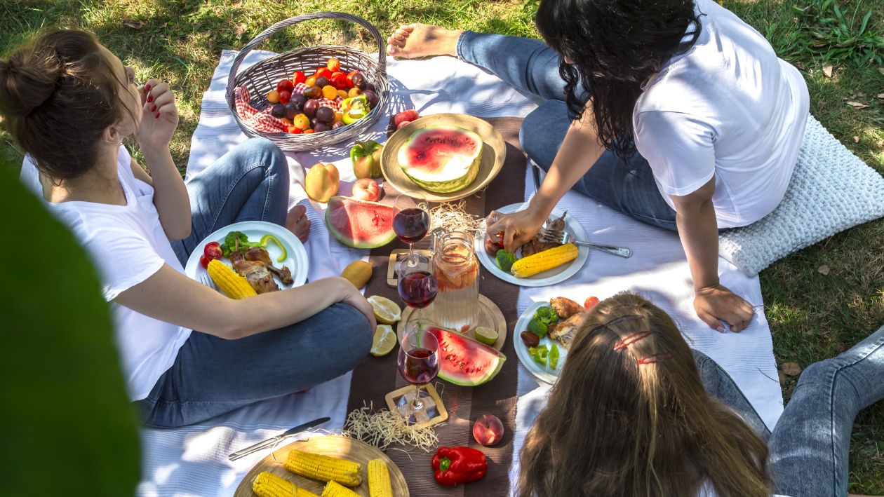 Eine Familie sitzt auf einer Picknickdecke und isst leckeres Obst