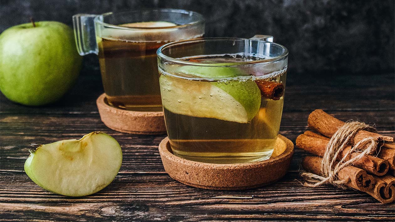 Drink in durchsichtiger Tasse mit Apfelspalten und Zimstangen