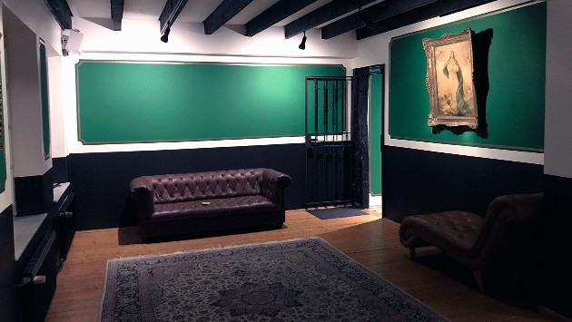 Man's World Lounge Innenansicht, eine gemütliche Couch steht vor einer dunkelgrün gestrichenen Wand