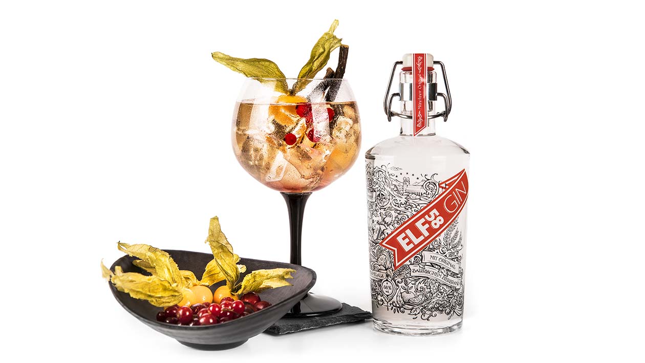Flasche ELF58 Gin mit Drink und Schale, dekoriert mit Beeren und Physalis