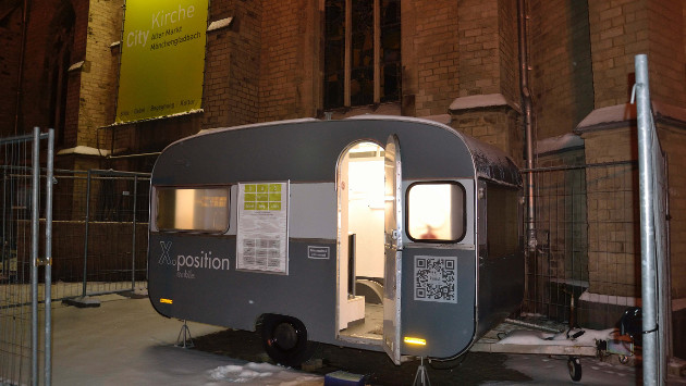 Ein kleiner Wohnwagen des Projekts X.position steht vor der Citykirche