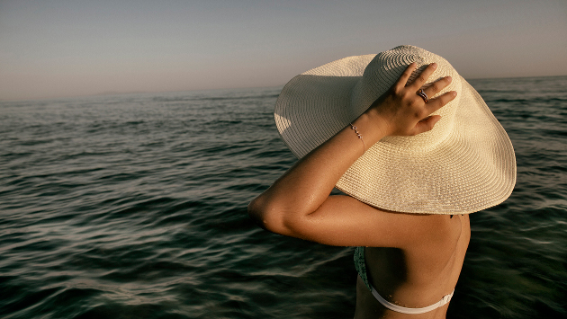 Eine Person im Bikini steht im Meer, sie trägt einen großen weißen Sonnenhut