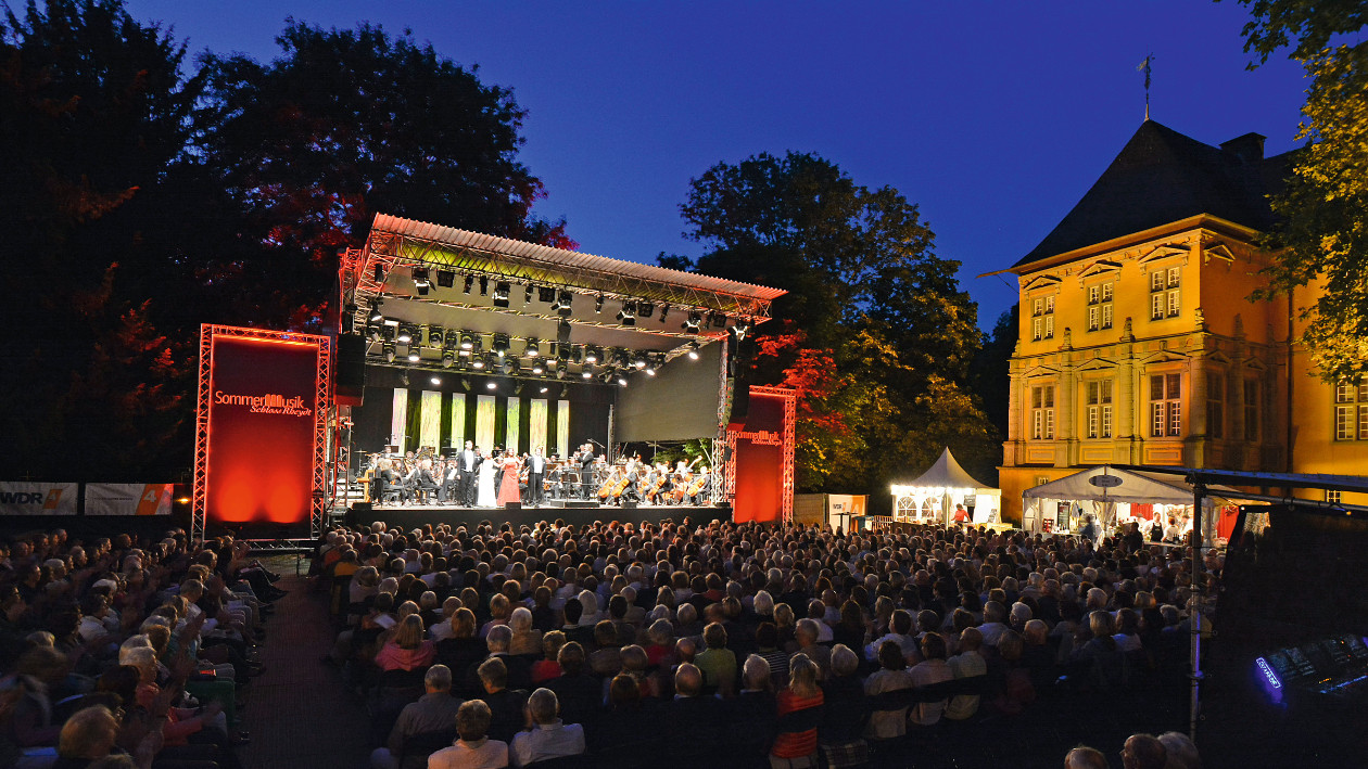 Eine Bühne steht vor dem Schloss Rheydt. Zuschauer hören der Band auf der Bühne zu.