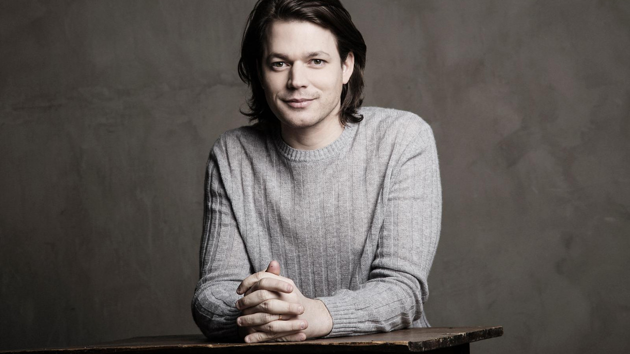 Pianist David Fray sitzt mit zusammengefalteten händen an einem Tisch