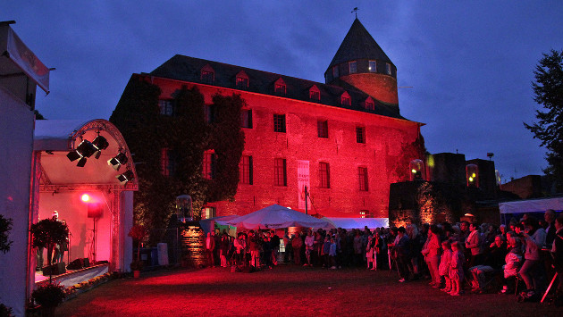 Die Burg Brüggen wird rot beleuchtet, im Innenhof stehen viele Menschen