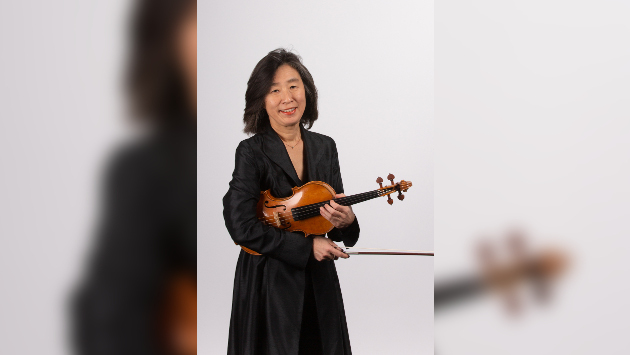Chisato Yamamoto steht vor einem Weißen Hintergrund und hält ihre Violine fest.