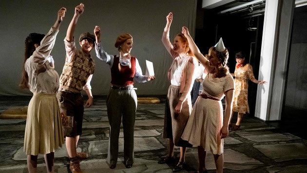 Eine Szene aus dem Theaterstück "Durch die Zeit Stolpern", mehrere Schaupieler stehen auf der Bühne im Kreis und halten die Hände hoch