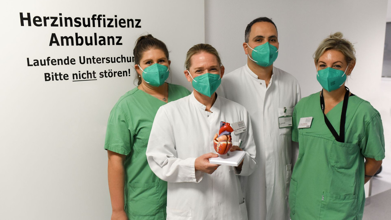 Selina Besancon, Diana Waldfried, Dr. Mirja Neizel-Wittke und Dr. Abdelouahid Azaouagh stehen vor einer Wand, welche den Schriftzug "Herzinsuffizienz Ambulanz" trägt.