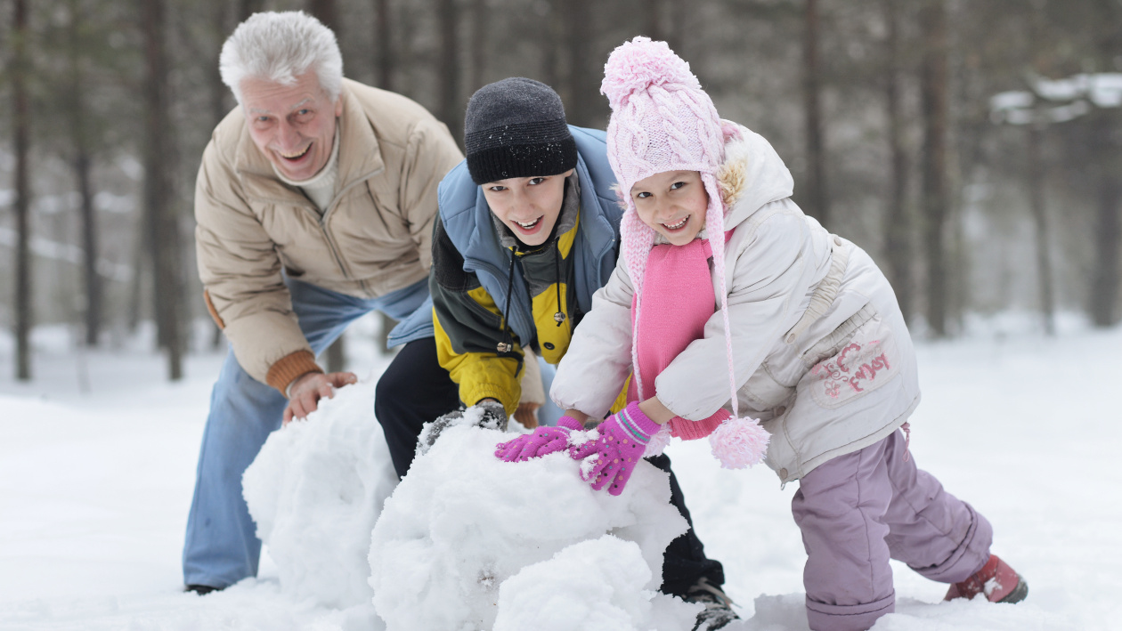 Ein Mann, ein Teenager Junge und ein kleines Mädchen rollen zusammen große Schneekugeln.