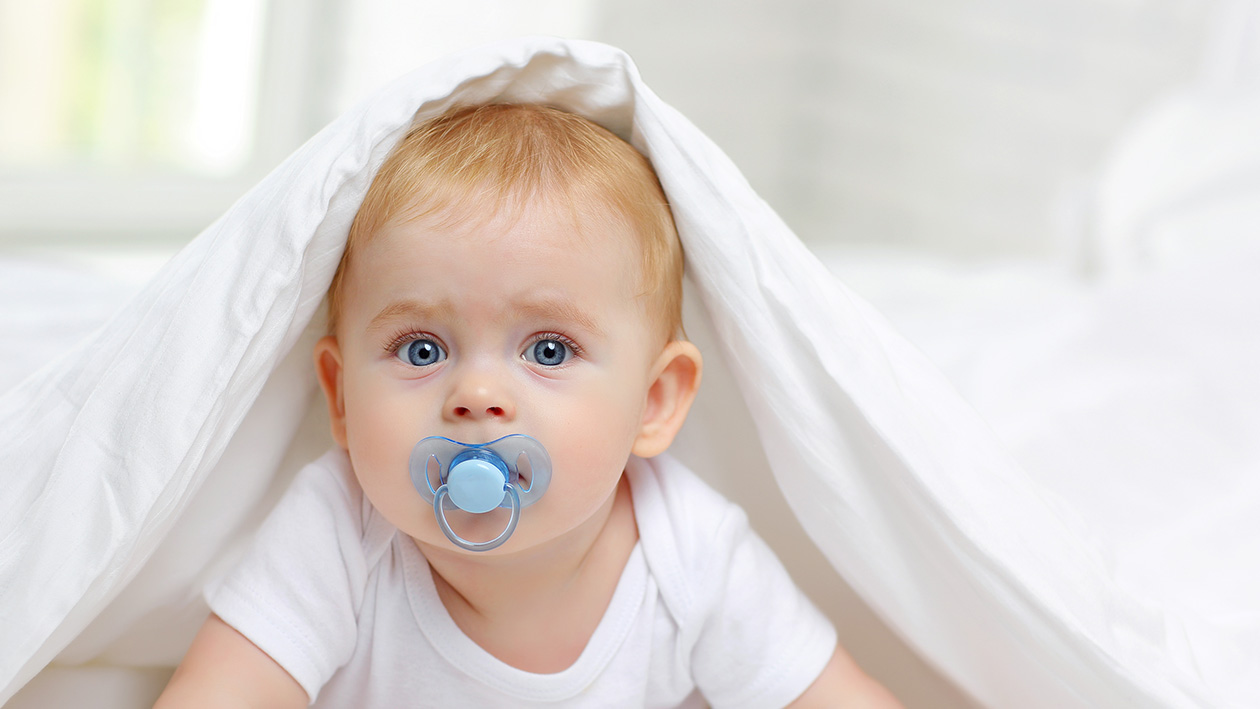Ein Baby mit einem Schnuller liegt unter einer Bettdecke