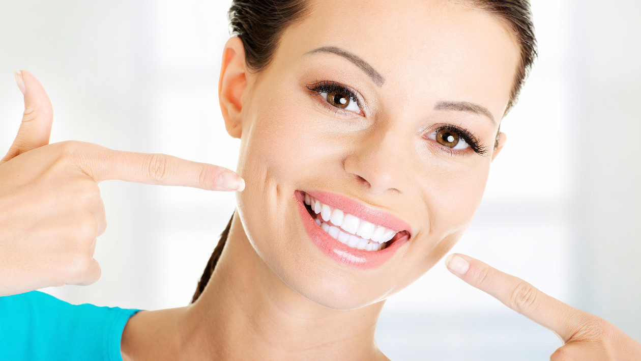 Eine lächelnde Frau, deren Zähne man sieht. Sie zeigt auf ihren Mund.